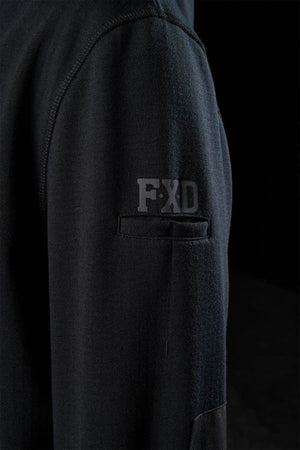 Close-up of a black FXD WF-3 Jacket sleeve shows a small pocket with the "FXD" logo above it. The dark background emphasizes the textured, high-quality design details characteristic of the FXD WF-3 Jacket.
