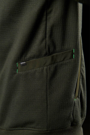 Close-up of a dark olive green FXD WF-3 Jacket pocket, featuring green stitching and a small black "Gunā 360" tag on the top edge, highlighting detailed workwear craftsmanship.