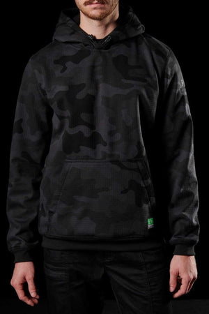 A person is wearing an FXD WF-1 Hoodie in black and gray camouflage, featuring a front pocket with a small green tag, paired with black pants. The dark background accentuates the individual's attire, making it the focal point of the image.