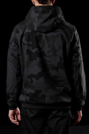 A person wearing an FXD WF-1 Hoodie made of black DURA500™ canvas with a dark camouflage pattern is seen from the back. They are also wearing black pants. The completely black background makes their clothing blend in slightly.