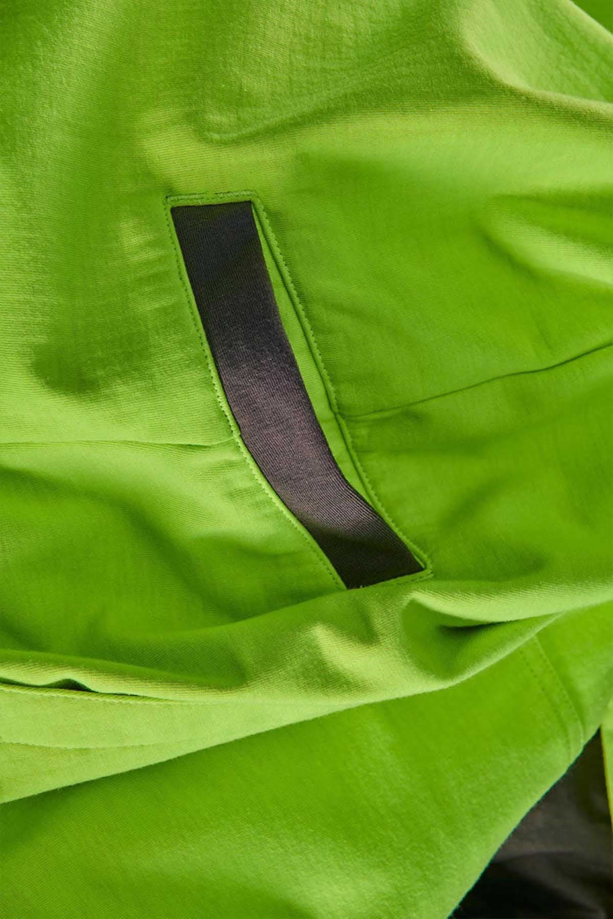 Close-up photo of the FXD WF-1 Hoodie’s bright green fabric with a black slit pocket. The material appears smooth and lightweight, possibly nylon or a similar synthetic, suggesting it could be water-resistant.