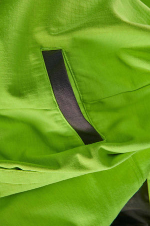 Close-up photo of the FXD WF-1 Hoodie’s bright green fabric with a black slit pocket. The material appears smooth and lightweight, possibly nylon or a similar synthetic, suggesting it could be water-resistant.