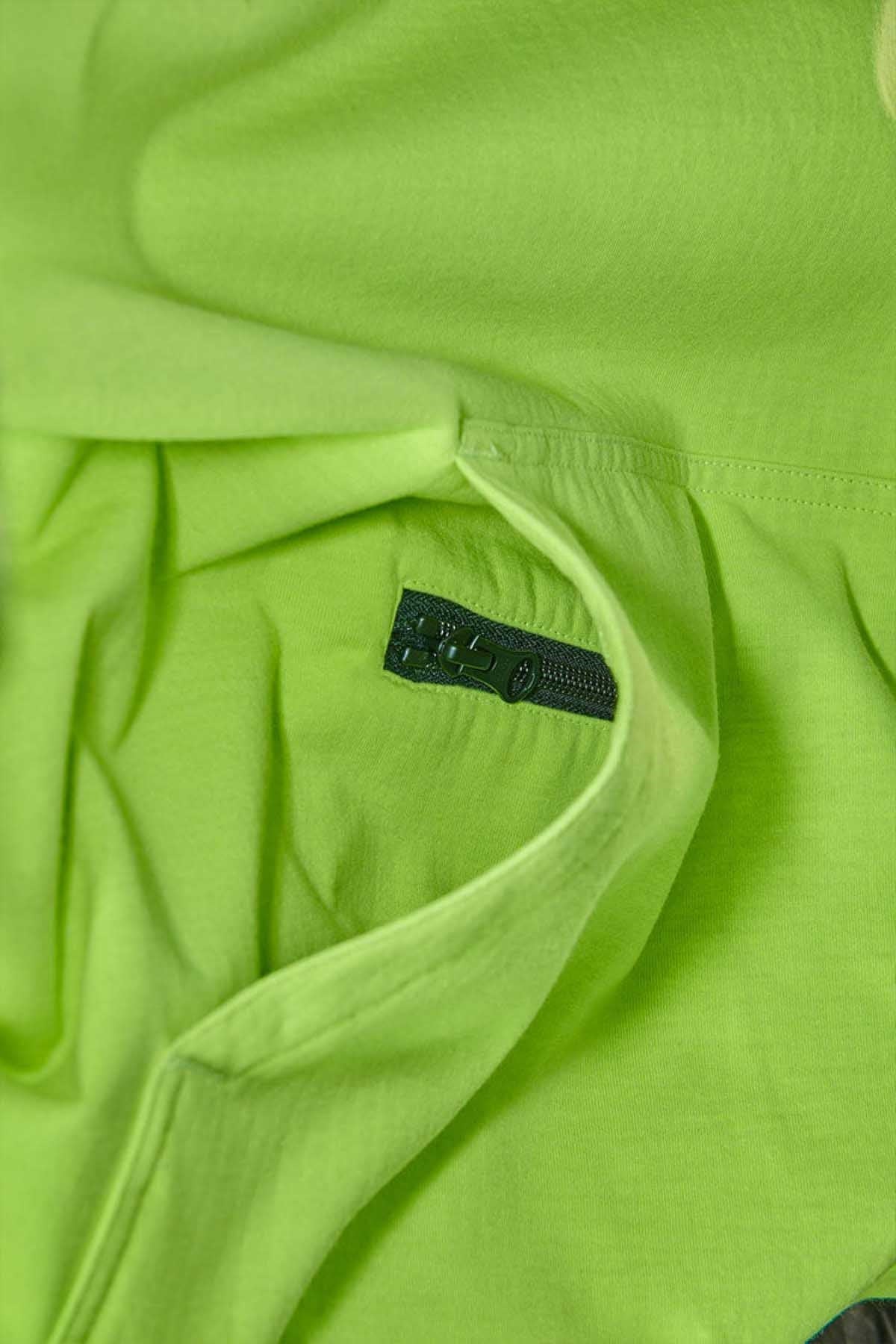 Close-up of the FXD WF-1 Hoodie's neon green fabric with a black zipper partially unzipped, revealing a pocket. The texture of the fabric is smooth, making it ideal for a water-resistant hoodie.