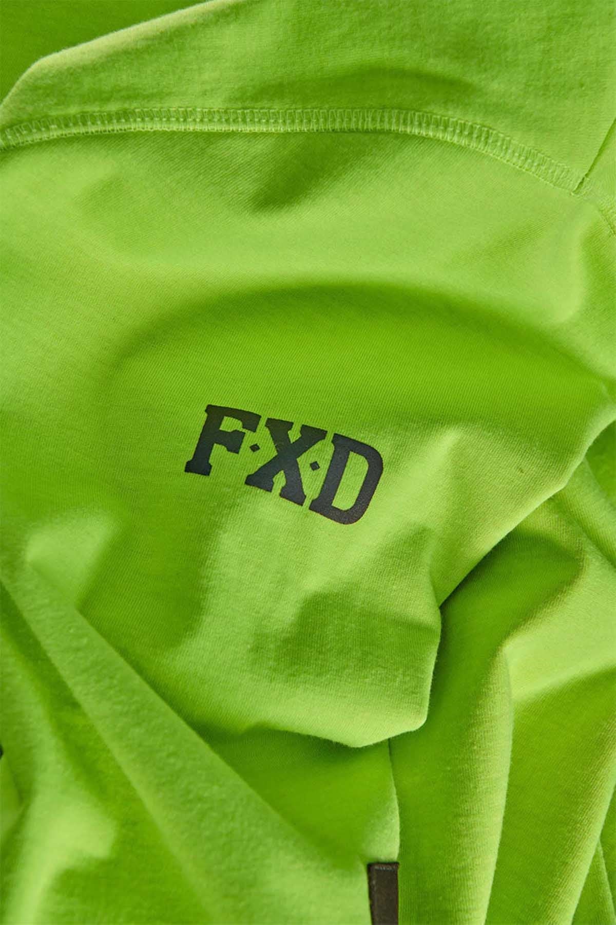 A close-up view of a green fabric with the letters "F X D" printed in bold black font on it. The FXD WF-1 Hoodie, featuring water-resistant material and visible seam detailing, suggests it is part of a garment, likely a t-shirt or hoodie.