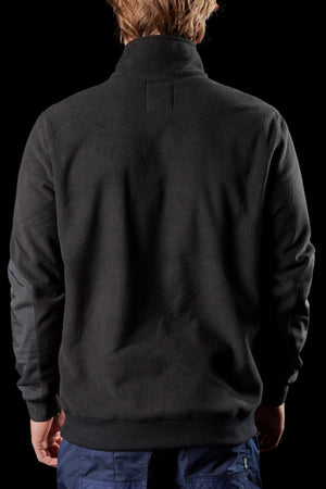 A person with light brown hair is shown from behind, wearing the FXD WF-2 Fleece jacket in black and dark blue pants against a solid black background.
