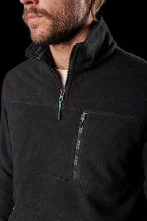 A bearded man wears the FXD WF-2 Fleece, a black windproof pullover with a quarter-zip collar and zippered chest pocket. Only his lower face and torso are visible against a black background.
