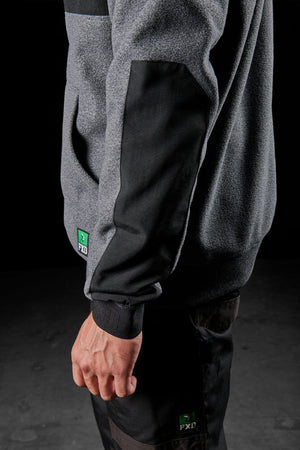 A person wearing the FXD WF-2 Fleece hoodie with reinforced black elbow patches and dark pants stands against a dark background. The green FXD logo is visible on both the windproof fleece jacket and pants.
