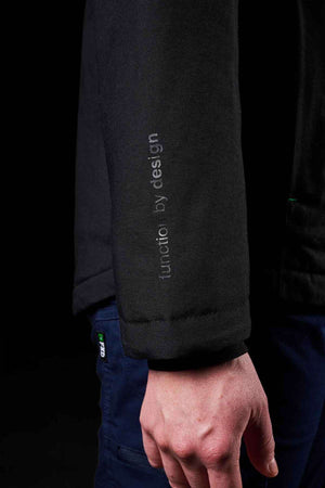 A close-up of a person’s arm in the FXD WO-1W Womens Insulated Work Jacket, featuring a durable black nylon sleeve with “function by design” printed vertically. The person wears dark blue pants against a black background.