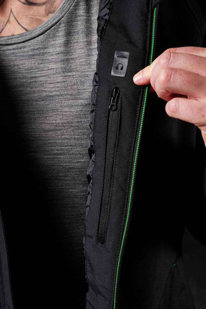 A person wearing a gray shirt unzips the FXD WO-1W Womens Insulated Work Jacket, revealing a small zippered pocket and a plastic loop inside. Only the person's torso and hand are visible.