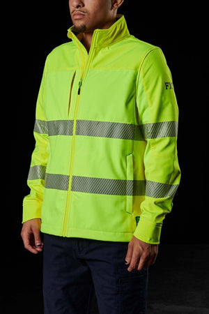 Against a dark backdrop, a person wears the FXD WO-3T Hi Vis Soft Shell Work Jacket, zipped up in bright yellow with reflective gray stripes. Known for wind and water resistance, the jacket features "FXR" on the sleeve. They pair it with dark pants.