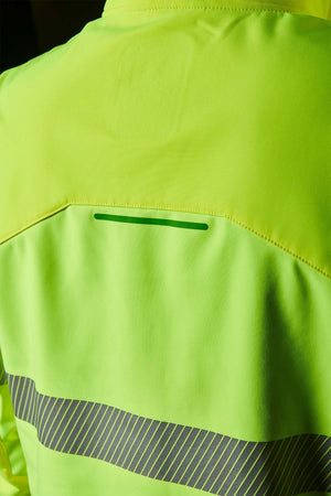 A person wears the FXD WO-3T Hi Vis Soft Shell Work Jacket in neon yellow with reflective stripes, showcasing its smooth, slightly shiny wind and water-resistant fabric under the light.