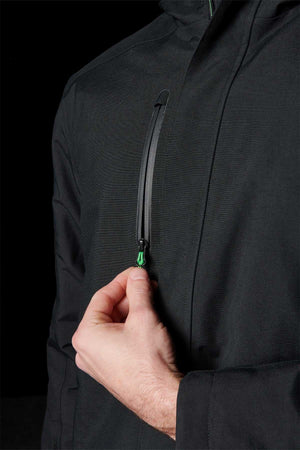 A person’s hand is pulling the zipper on a vertical chest pocket of a black FXD WO-1 Insulated Work Jacket, against a dark background.