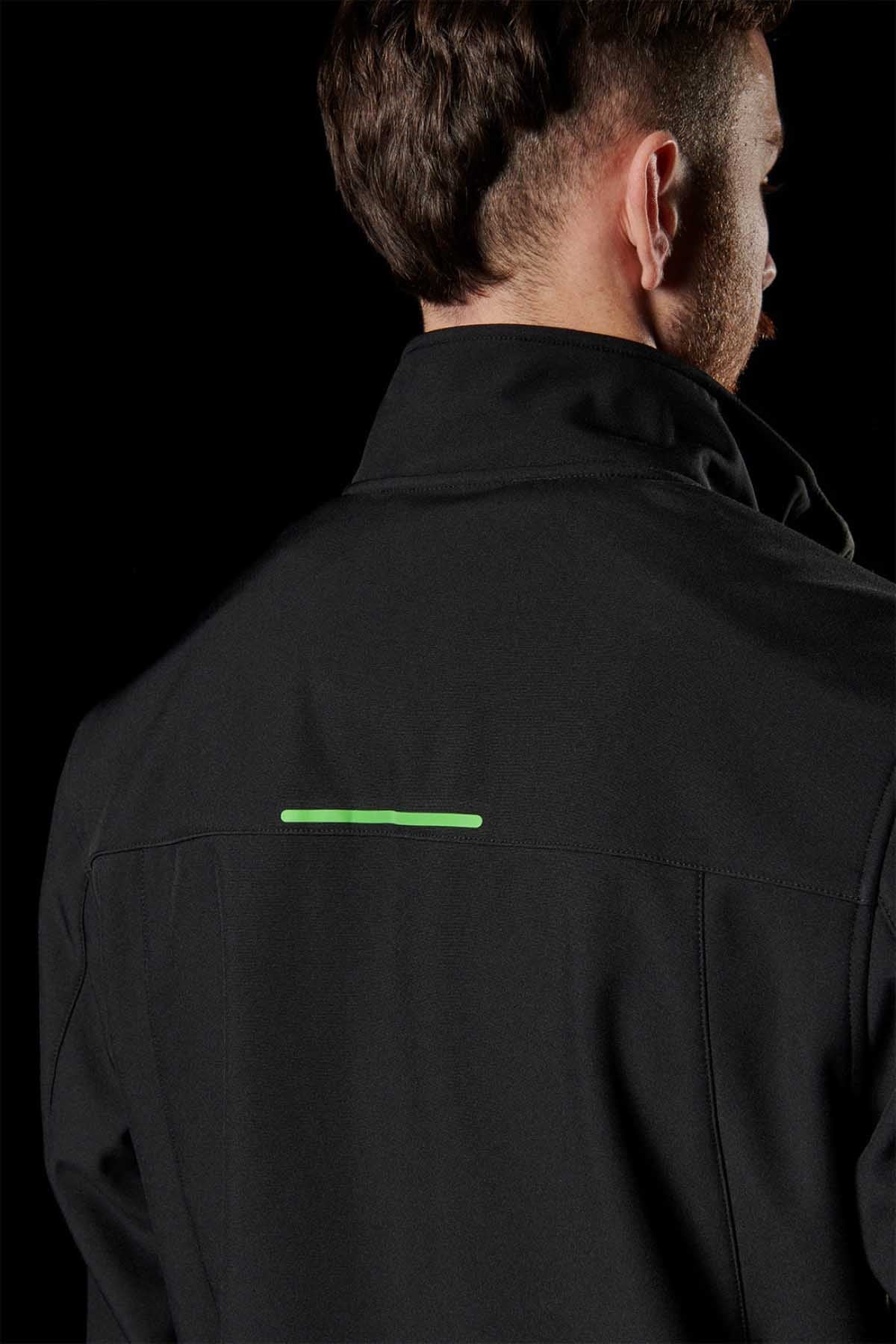 A person with short brown hair is shown from behind wearing a sleek FXD WO-3 Soft Shell Work Jacket in front of a dark background. The black, breathable jacket features 50+ UPF protection and has a small green reflective strip near the shoulder blades; it is wind and water-resistant.