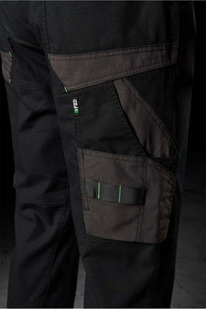 Close-up of FXD WP-11 work pants in black with dark grey accents, showcasing multi-functional cargo pockets and a green and white "PRO" label. These pants feature a robust design with 2-way stretch fabric ideal for heavy-duty tasks, reinforced stitching, and practical storage solutions. The background is dark.