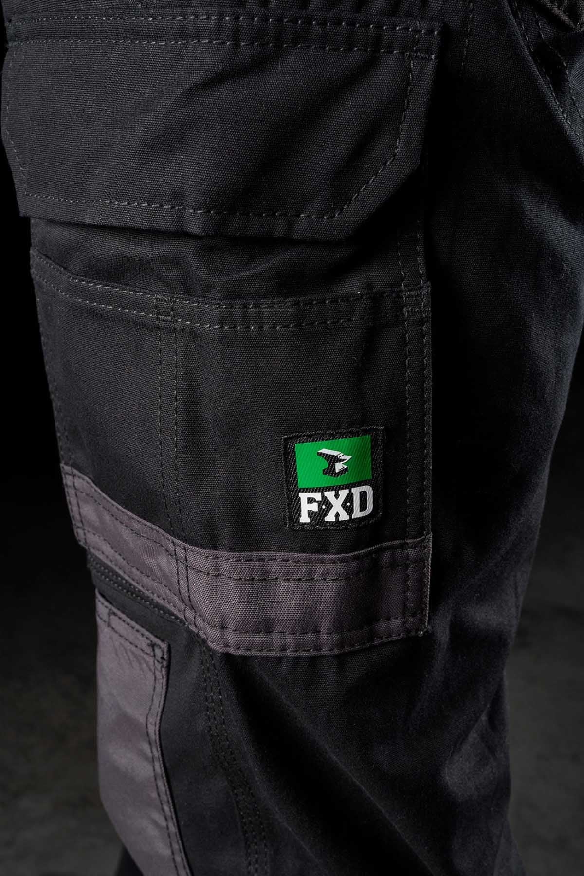 Close-up of an FXD WP-1 black work pant pocket, featuring gray stitching and a green and black FXD logo patch. The texture of the fabric and stitching details are visible, indicating rugged, durable construction with 360 degree stretch and Duratech reinforced pockets suitable for heavy-duty work environments.