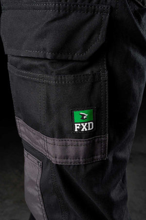 Close-up of an FXD WP-1 black work pant pocket, featuring gray stitching and a green and black FXD logo patch. The texture of the fabric and stitching details are visible, indicating rugged, durable construction with 360 degree stretch and Duratech reinforced pockets suitable for heavy-duty work environments.