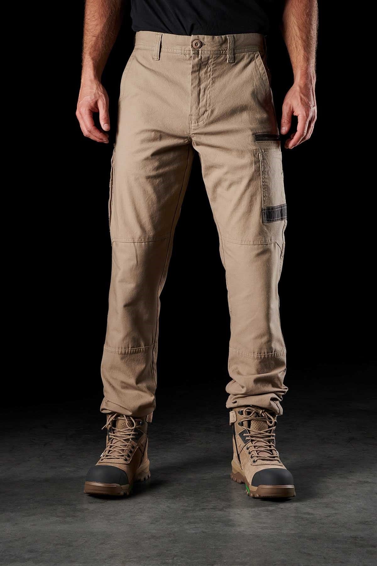 A person is wearing FXD WP-3 khaki cargo pants with reinforced pockets and brown lace-up boots. The image shows the person from the waist down, highlighting the FXD WP-3's multiple pockets and the rugged design of the boots. The background is black, emphasizing the clothing and footwear.