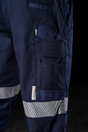 Close-up shot of a navy blue FXD WP-3T work pant pocket featuring multiple compartments and a small zippered section. The pant has white and blue striped reflective tape near the knee area for added visibility. The pocket, boasting an embroidered label with a green symbol and text, offers 360-degree stretch. Background is black.