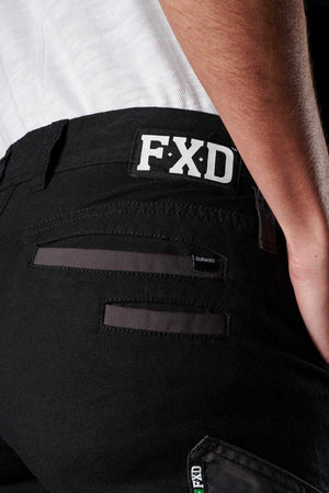 Close-up of a person wearing black FXD Womens WP-4W stretch work pants, showing the back pocket area with "FXD" branding above the right pocket and a "DURA500" tag on the DURA500 reinforced pocket flap. The person is also wearing a white shirt.