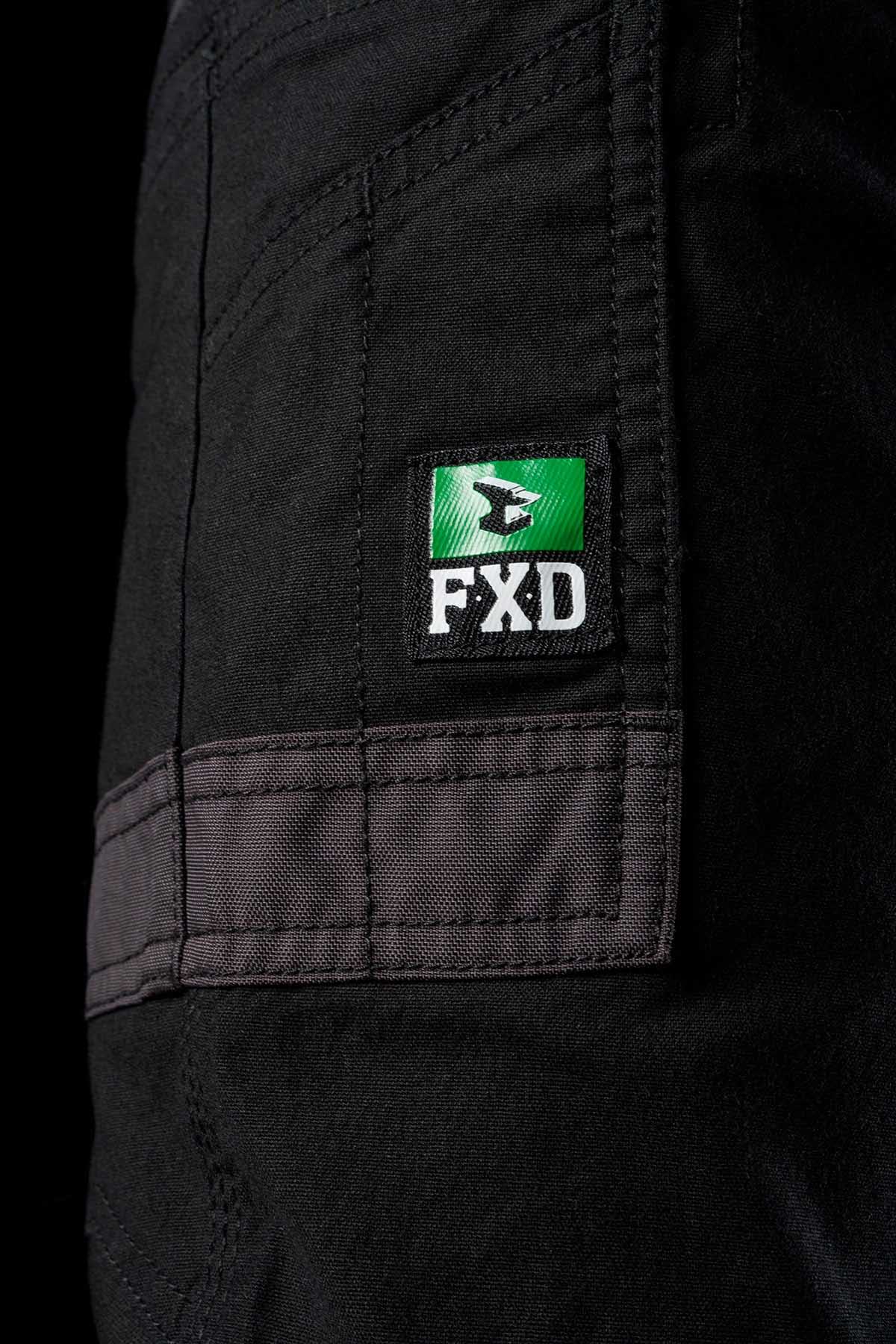 A close-up view of the FXD Womens WP-4W workwear pants, showcasing DURA500 reinforced pockets and a distinct green and white FXD logo patch. Made from durable stretch Cotton Twill, these black pants feature reinforced seams, with the completely black background highlighting the fabric and stitching details.