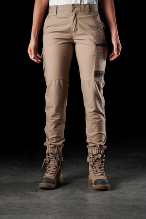 A person standing against a dark background is wearing FXD Womens WP-4W beige cotton twill cargo pants with multiple DURA500 reinforced pockets and brown lace-up boots. The pants are gathered at the ankles, and the person's hands are hanging by their sides.