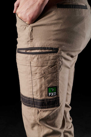 Close-up of a person wearing FXD Womens WP-4W beige stretch work pants with black details and multiple DURA500 reinforced pockets. The side pocket prominently features a green and black FXD logo.