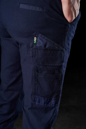 A close-up of a person wearing FXD Womens WP-4W navy blue cargo pants made from Cotton Twill. The image highlights multiple reinforced pockets, including a large one on the thigh with smaller stitched compartments on the front. The person's hand rests casually in the front pocket.