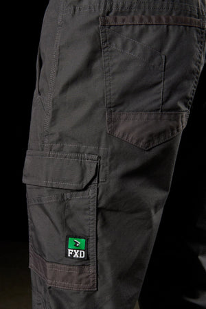 Close-up image of the FXD WP-5 dark-gray work pants featuring multiple pockets made from ultra-durable advanced stretch fabric. A green and white label with the text "FXD" is visible on the side pocket. The stitching details and texture of the fabric are highlighted against a black background.