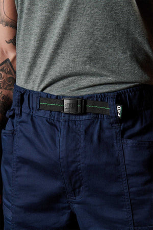 The individual wears a gray shirt and FXD WP-6 dark blue work pants made from stretch nylon twill. A tattoo is visible on their arm. The small belt has a rectangular metal buckle, and green stitching accents the waistband stylishly.
