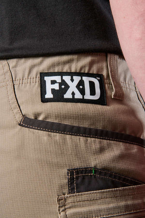 Close-up of an individual sporting the FXD WS-6 Work Short in beige, showcasing a black patch with "FXD" lettering on the back pocket. Renowned for their comfort and practicality, these shorts feature visible stitching and a loop located above the pocket.