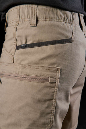 A close-up of an individual wearing FXD WS-6 Work Shorts showcases features such as the pockets and black trim. The fabric looks durable and textured, capturing both comfort and practicality. The dark background perfectly highlights these beige cargo shorts.