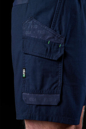 A close-up of an individual wearing the durable FXD WS-7 Work Short in dark blue, featuring a patterned pocket. The pocket includes a flap with visible branding and a green tag. Crafted for comfort, the fabric showcases a subtle textured design.