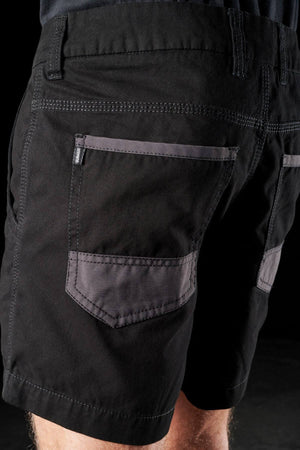 Close-up of the back of a person wearing FXD WS-2 Short Shorts in black, showcasing the gray, patch-style back pockets. The detailed stitching and seams are clearly visible, with abrasion panels adding to the shorts' durability. Set against a dark background, only the lower back and upper legs are shown.