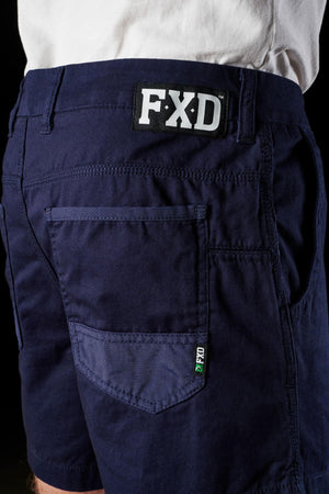 Close-up of a person wearing FXD WS-2 Short Short in dark blue, shown from the back. The stylish shorts feature multiple pockets, including a visible back pocket with a small green tag on the side. The person is also wearing a white shirt, partially visible at the top.