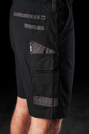 A close-up of a person wearing the FXD WS-3 Shorts made from black stretch cotton canvas, showcasing multiple zippered and velcro pockets. The image focuses on the thigh and hip area, emphasizing the practical design with triple needle seams and detailed stitching against a dark background.