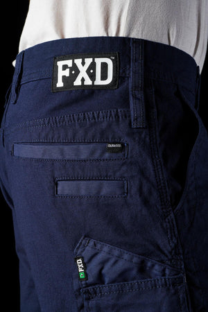 Close-up view of the back pocket of dark blue FXD WS-3 Shorts, showcasing a white "FXD" label above the pocket. The stretch cotton canvas fabric, with multiple stitching lines and an "FXD" tag on the lower seam, offers both comfort and durability. The material appears resilient and built for heavy-duty use.