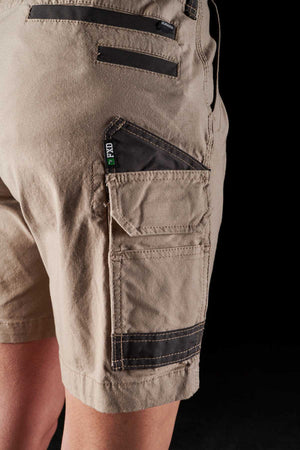 Close-up photo of a person wearing tan FXD Womens WS-3W Shorts with multiple DURA500 reinforced black and tan pockets on the side, designed for holding tools or accessories. The background is black, drawing attention to the detailed design and stitching of the stretch work short.