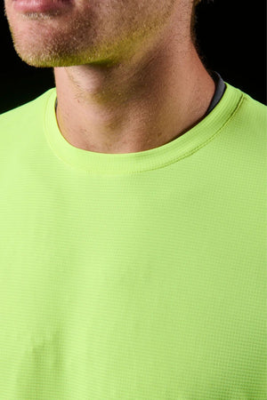 A close-up of a person wearing the textured, bright yellow-green FXD WT-4 Hi Vis Tech Tee, revealing their lower face, neck, and upper chest against a dark background.