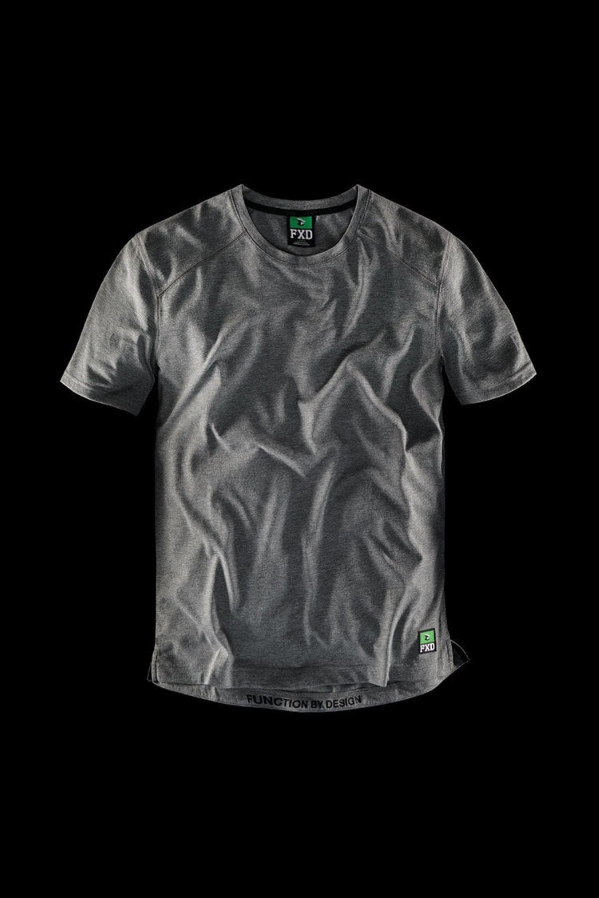 The FXD WT-3 Tech Tee, in a charcoal grey color with short sleeves and a naturally wrinkled appearance, is showcased against a black backdrop. Crafted from recycled polyester, the shirt features a small green and black label near the hem and has a circular neckline. The text "FXD" and "Function by Design" is prominently displayed on the tee.