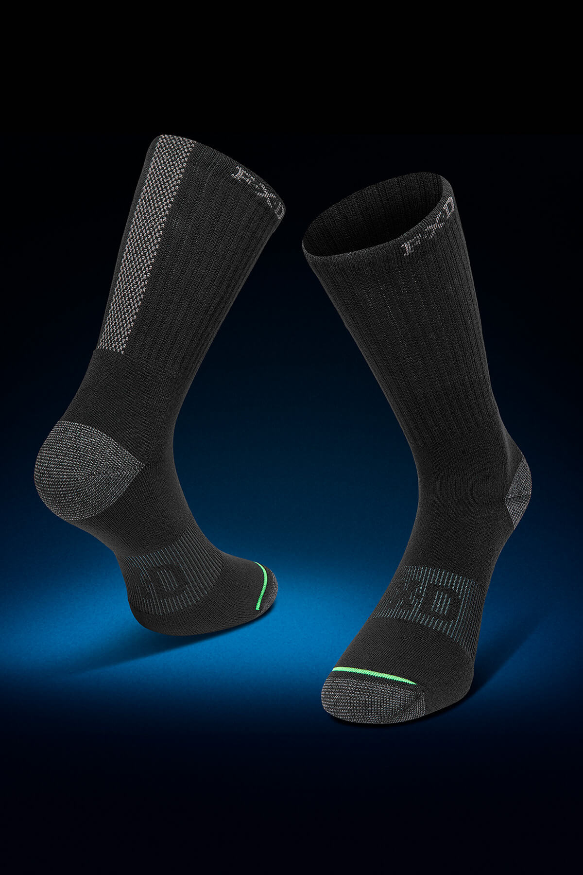 A set of black and gray socks from the FXD SK-8W Crew Sock 5 Pack is showcased against a dark gradient background. These socks boast ribbed cuffs, a padded foot bed, integrated arch support, and padded heel and toe areas. Subtle jacquard logos along with green stitching details can be seen near the toes.