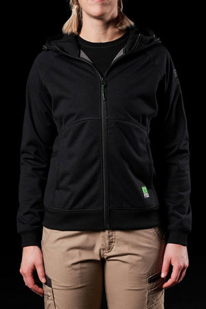 Against a black backdrop, the person wears a sleek FXD Womens WF-3W Jacket. This black zip-up hoodie features a hood, paired with tan cargo pants. Their relaxed stance highlights the jacket's windproof comfort and water-resistant versatility, exuding confidence and style.