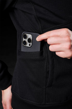 Sporting a FXD Womens WF-3W Jacket, a person partially tucks a smartphone into their pocket, showcasing its striking triple-lens camera module. The jacket combines style with water resistance for versatile conditions.