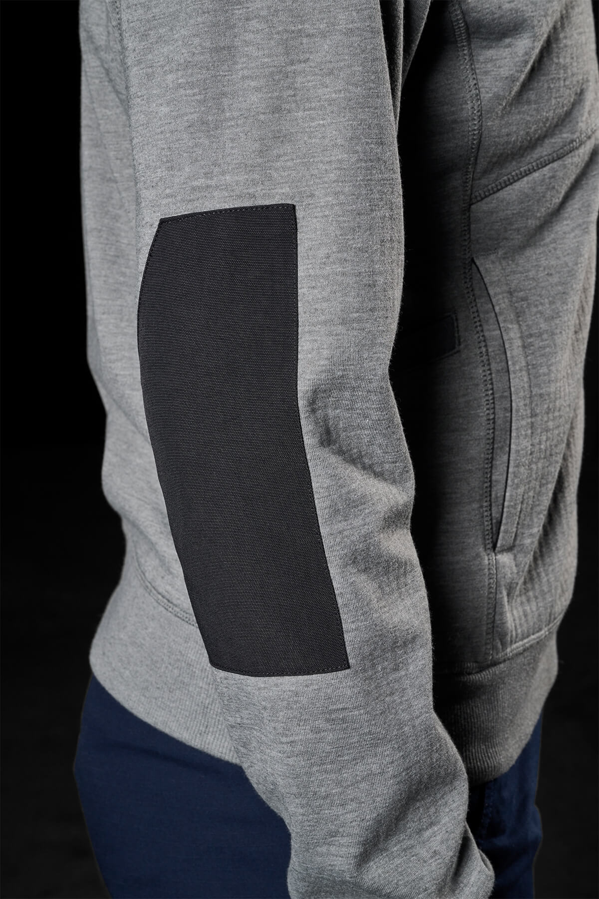 A close-up view of a person wearing a grey sweatshirt with a black elbow patch, showcases the textured fabric of the sleeve against a dark background. The visible pocket seams evoke the design of the FXD Womens WF-3W Jacket, renowned for its water resistance and windproof qualities.