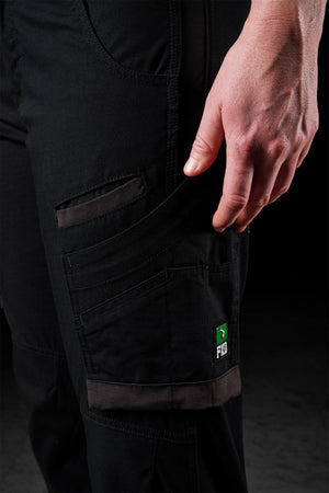 A close-up of a person wearing black FXD Womens WP-7W work pants with several pockets. The left hand rests by the side, and a small patch with the letters "FHD" and a green symbol is visible on one of the pockets. These flex double weave pants provide 50+ UPF protection, against a dark background.