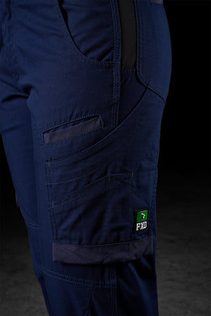 Close-up of FXD Womens WP-7W pants in dark blue, showcasing multiple pockets, a Velcro flap pocket, and a tool compartment. These work pants also feature reinforced stitching, flex double weave hip panels, and a small black and green FXD logo tag on the side. The background is dark and indistinct.