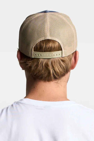 Reverse angle of someone sporting a FlexFit American Stitch Trucker Cap in beige, featuring contrast stitching and a snapback strap for custom fitting. The person, with short light brown hair, is dressed in a white shirt against a simple light gray background.
