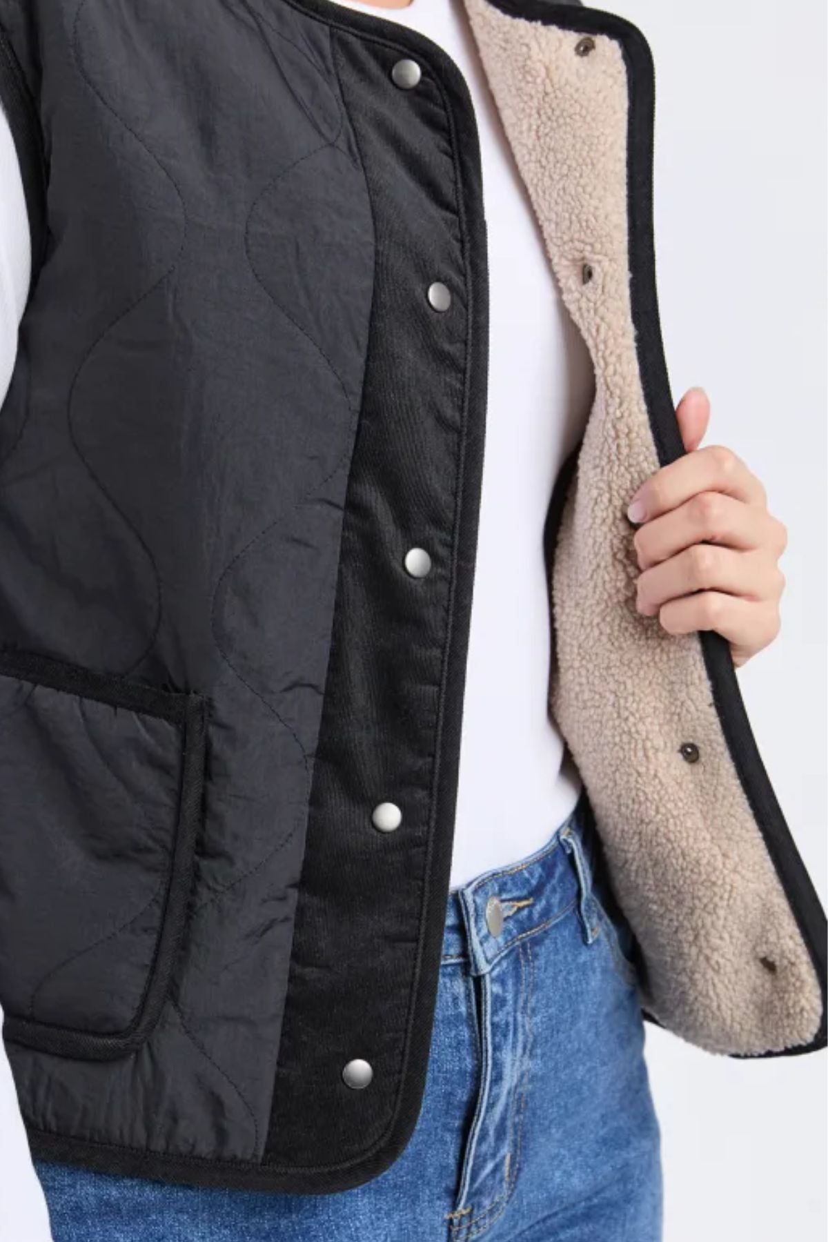 Wearing blue jeans and a white top, a person opens the Foxwood Alberta Vest with snap buttons, showing its cozy sherpa lining.