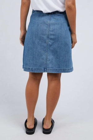 A person wearing a Foxwood Amanda Skirt and black slide sandals is standing with their back facing the camera against a plain background, exuding a subtle retro vibe.