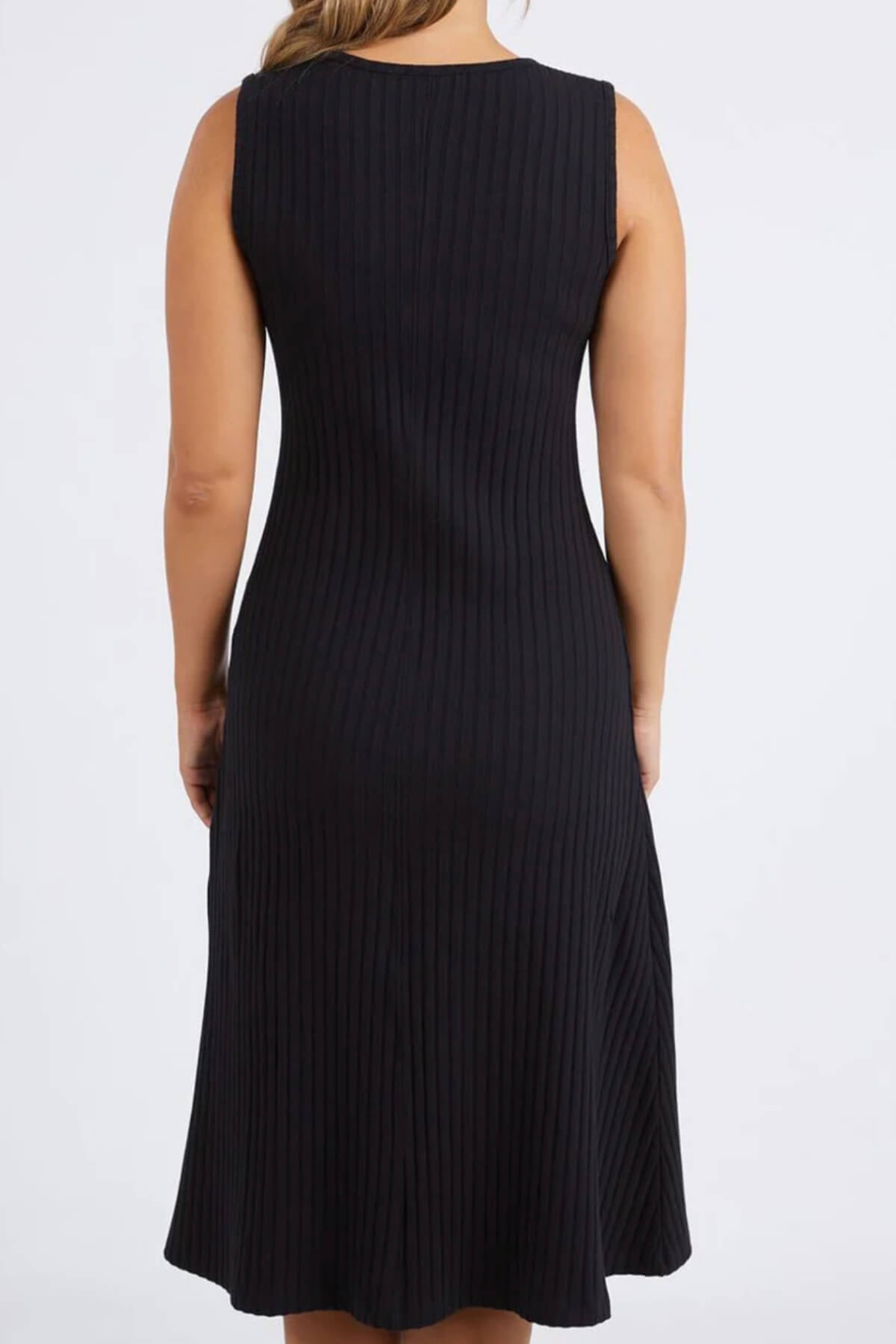 A woman models the Foxwood Amelie Rib Dress—a sleeveless, knee-length black dress made from 100% cotton rib—facing away to show its back against a plain light background.