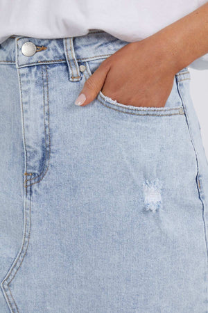 Close-up of a person wearing the Foxwood Belle Skirt. One hand is partially tucked into the front pocket of the skirt. The fabric exhibits a slightly distressed texture near the pocket, and the person is pairing it with a white shirt.